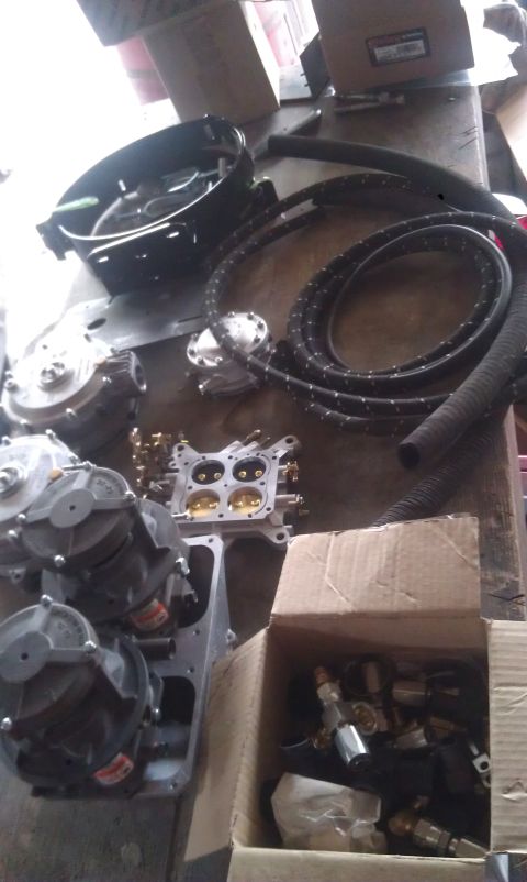 1978 Ford Bronco - Various engine parts, including a carburetor and fuel pumps, are spread across a workbench.