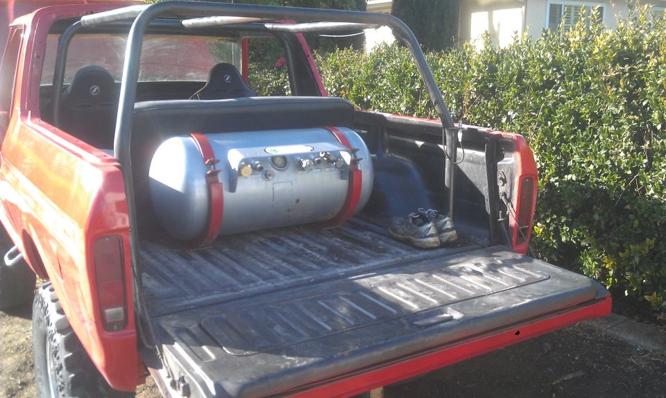 Red 1978 Ford Bronco rear view with a large silver propane tank and red straps in the cargo bed