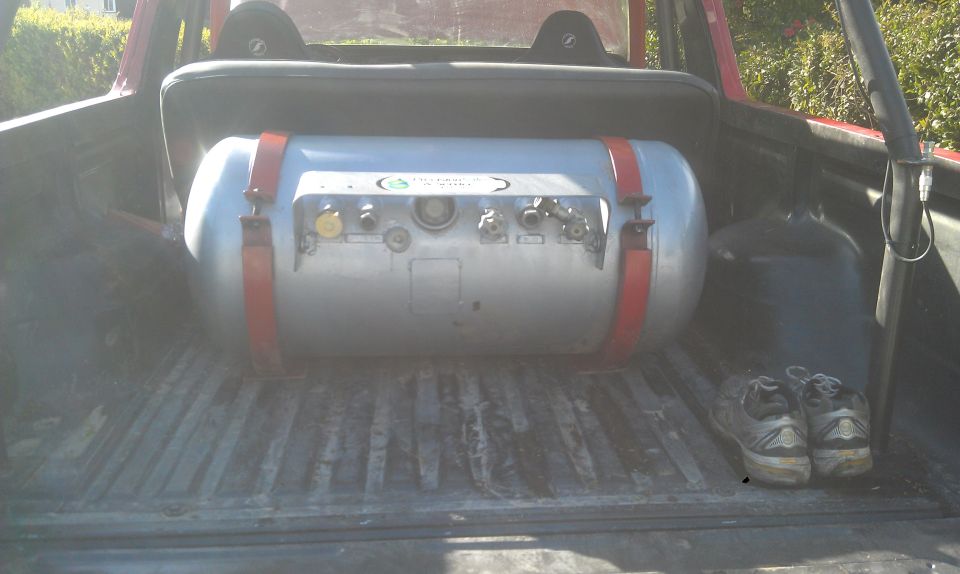 Propane tank with red straps in the bed of a red vehicle