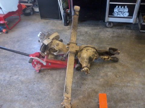 1995 Ford F-150 - Front axle assembly supported by a red hydraulic jack, likely for a vehicle modification or repair.