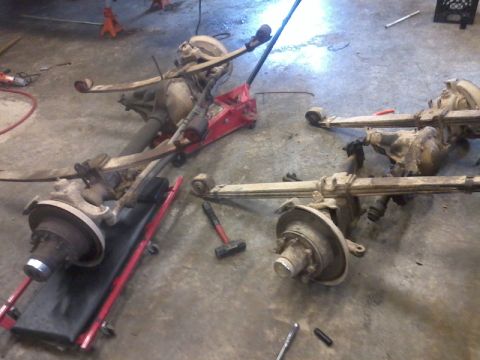 1995 Ford F-150 - Disassembled vehicle axles and suspension components are laid out on a concrete floor, possibly for repair or modification.
