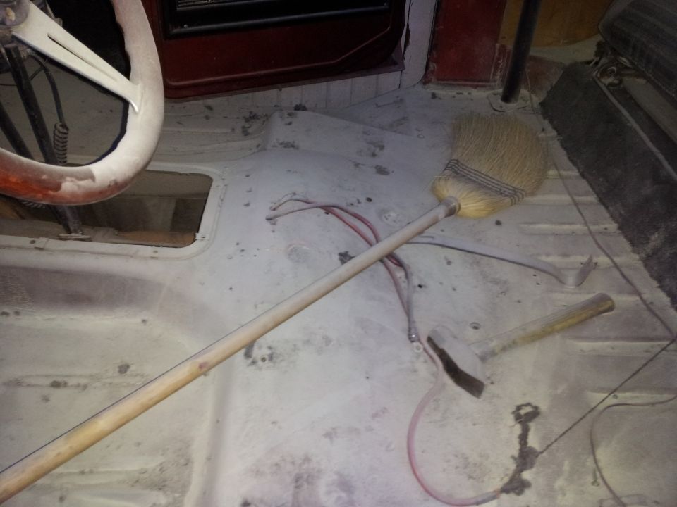Interior floor of a vehicle with a broom, hammer, and steering wheel visible
