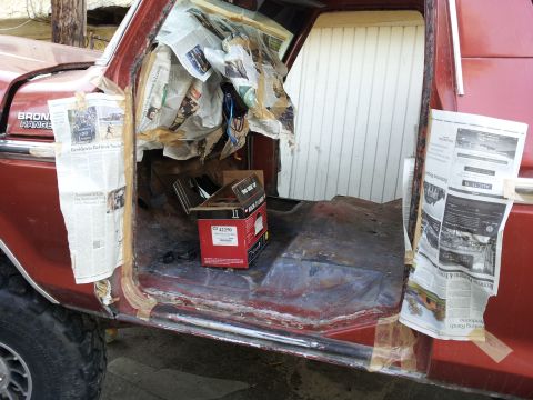 1978 Ford Bronco - The interior of a red 1978 Ford Bronco is shown with the door open, revealing newspaper used for protection and a box on the floor.
