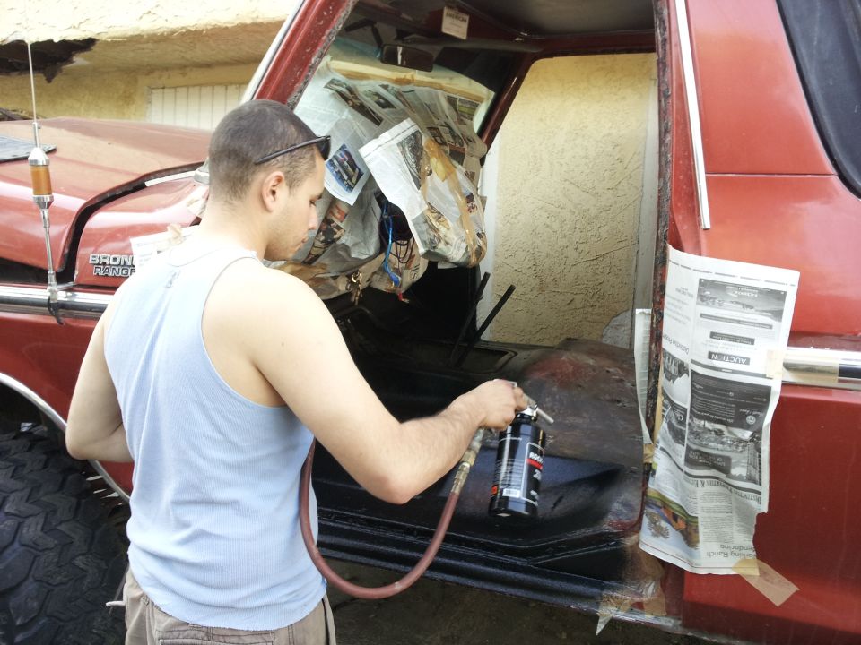 Man spraying inside a red 1978 Ford Bronco, interior is masked with newspaper