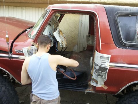 1978 Ford Bronco - A man works on the interior of a red Ford Bronco, with newspaper protecting the door frame.