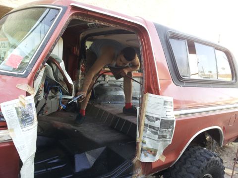 1978 Ford Bronco - A man works on the interior of a red 1978 Ford Bronco, with newspaper used as protective covering.