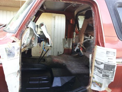1978 Ford Bronco - The interior of a red SUV is shown with the floor being painted and newspaper used to protect the dashboard during the work.