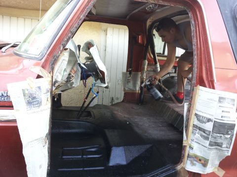 1978 Ford Bronco - Person spraying black paint onto the floor of a 1978 Ford Bronco interior.