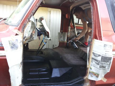 1978 Ford Bronco - A person is spraying the interior of a red truck, with newspaper protecting the surfaces.