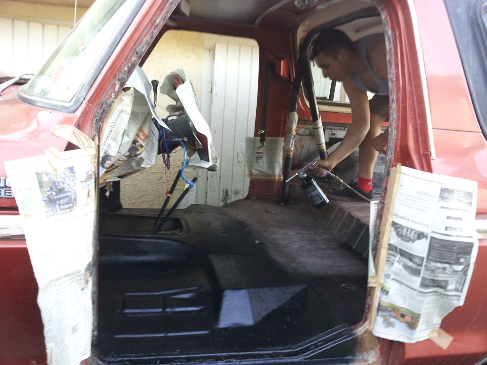 Person spraying something inside a red truck's interior, which is covered in newspaper