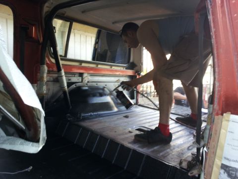 1978 Ford Bronco - A person sprays black coating inside the red interior of a vehicle, with a roll cage visible.
