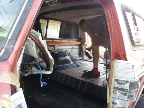 1978 Ford Bronco - A person sprays paint inside the cargo area of a 1978 Ford Bronco, with newspaper protecting the interior.