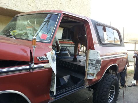 1978 Ford Bronco - A red 1978 Ford Bronco is shown with its doors removed, revealing the interior and a person working inside.