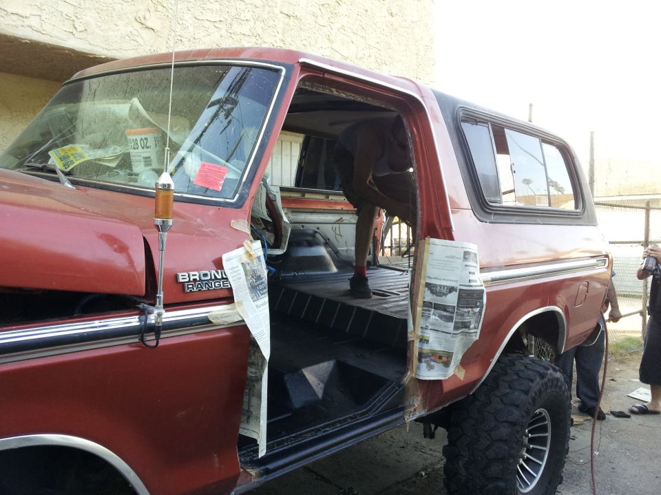 Red 1978 Ford Bronco with doors open, interior being worked on. Newspaper taped to door frames