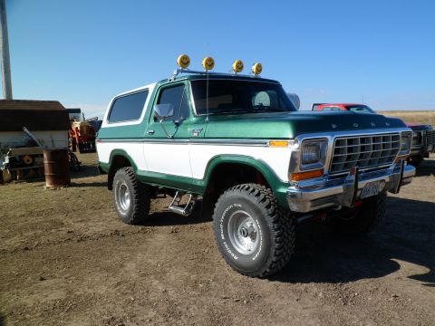 1979 Ford Bronco - A two-tone green and white Ford Bronco is parked outdoors under a clear blue sky, with other vehicles visible in the background.