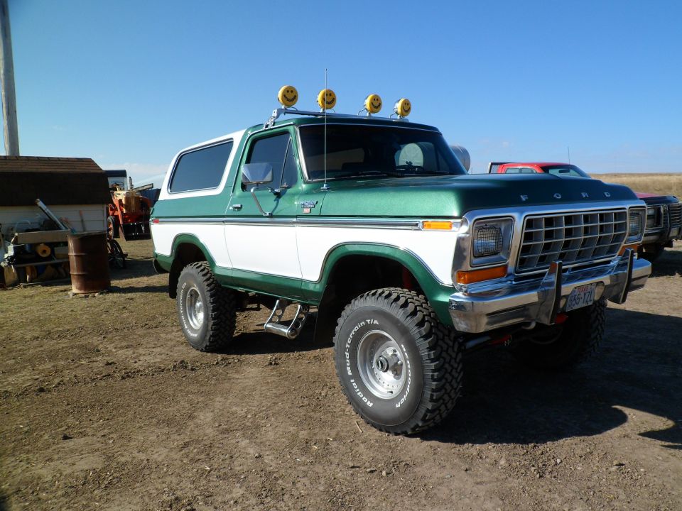 Green and white 1978 Ford Bronco with four smiley face lights on the roof, lifted suspension, and off-road tires
