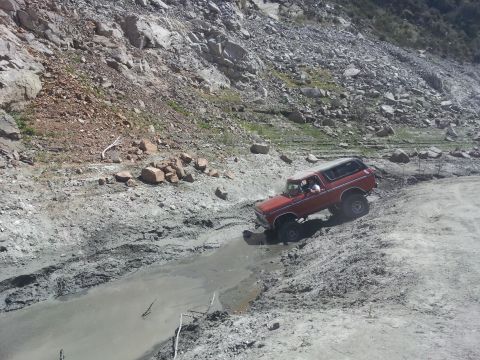 1978 Ford Bronco - A red 1978 Ford Bronco navigates a challenging muddy terrain on a steep, rocky incline.