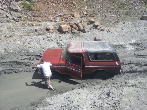 1978 Ford Bronco - A person attempts to free a red 1978 Ford Bronco that is deeply stuck in thick mud.