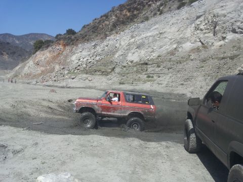 1978 Ford Bronco - Two off-road vehicles navigate a muddy, rocky terrain under a clear blue sky.