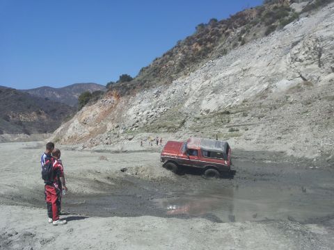 1978 Ford Bronco - A red 1978 Ford Bronco navigates a muddy off-road terrain, with onlookers observing the foreground.