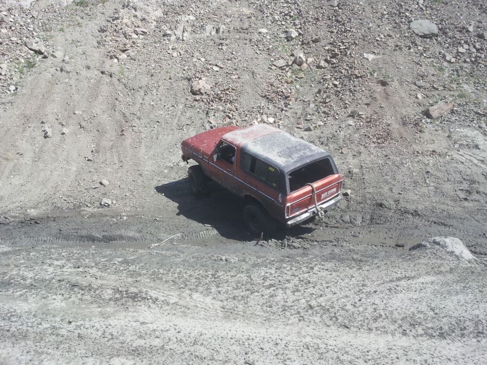 Red 1978 Ford Bronco with a black top, stuck in mud on a rocky incline