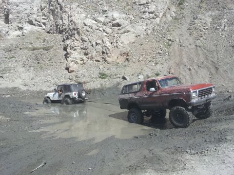 1978 Ford Bronco - Two off-road vehicles are stuck in a muddy area with a rocky hillside in the background.