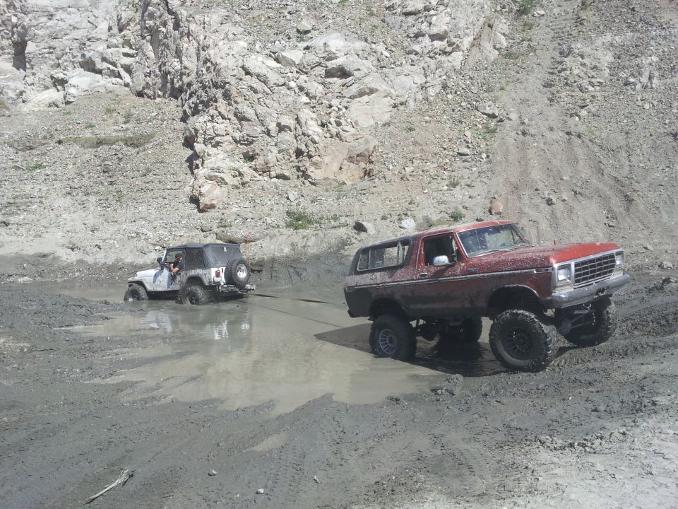 Red 1978 Ford Bronco pulling a white Jeep Wrangler out of a mud pit