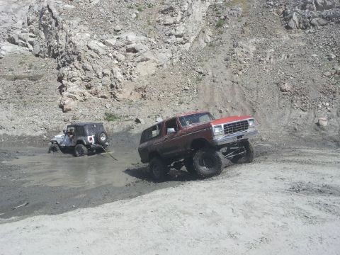 1978 Ford Bronco - A red 1978 Ford Bronco is being towed by a Jeep in a muddy, rocky terrain.