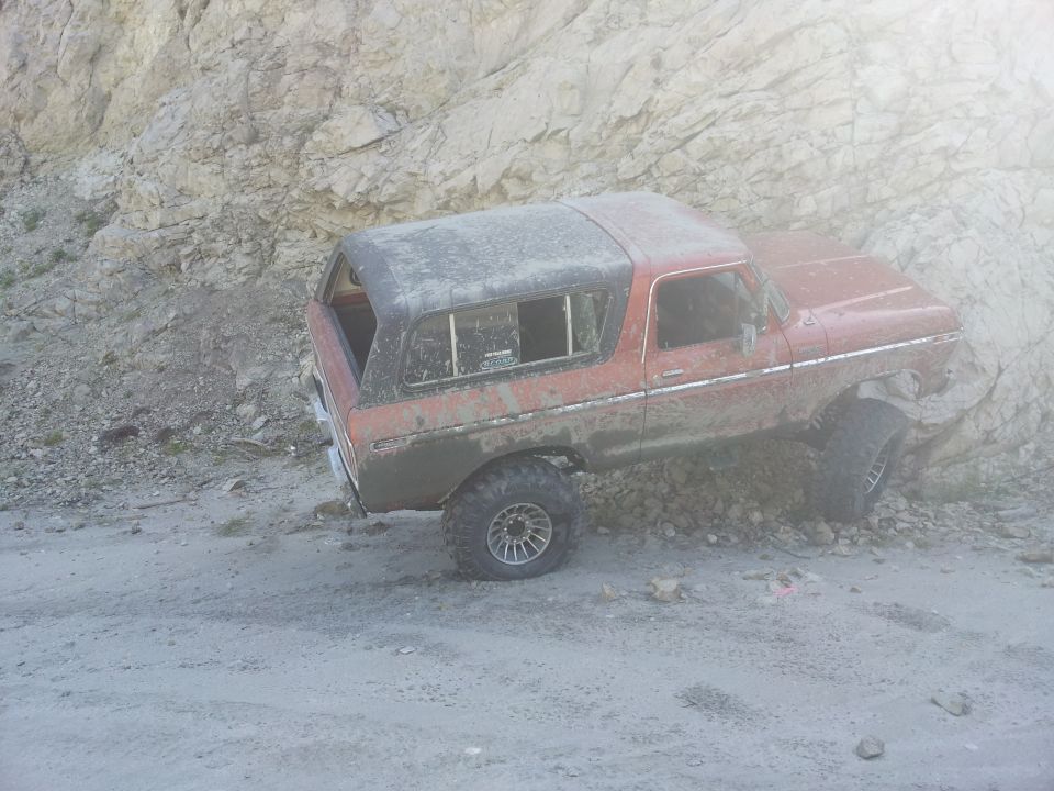 Red 1978 Ford Bronco on a dirt road next to a rocky incline