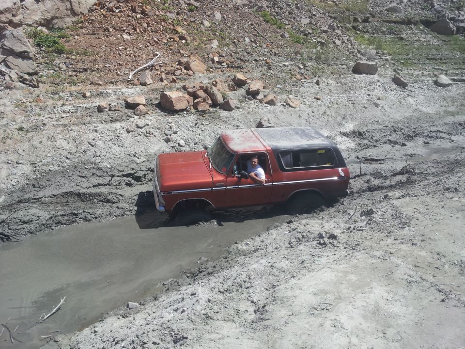 Red 1978 Ford Bronco navigating a muddy trail