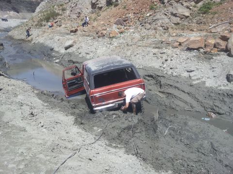 1978 Ford Bronco - A 1978 Ford Bronco is stuck deep in mud, with a person attempting to free it while another vehicle is visible in the background.