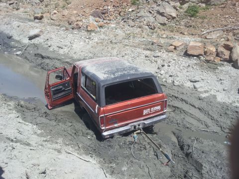 1978 Ford Bronco - A red 1978 Ford Bronco is stuck in a muddy ditch, its driver's door ajar.