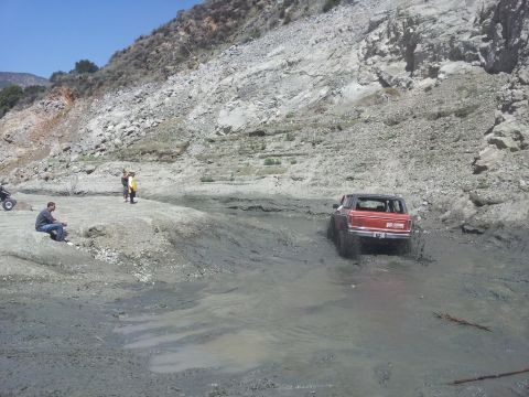 1978 Ford Bronco - A red 1978 Ford Bronco navigates a muddy terrain with a rocky hillside in the background.