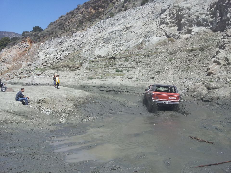 Red 1978 Ford Bronco driving through mud, rear view