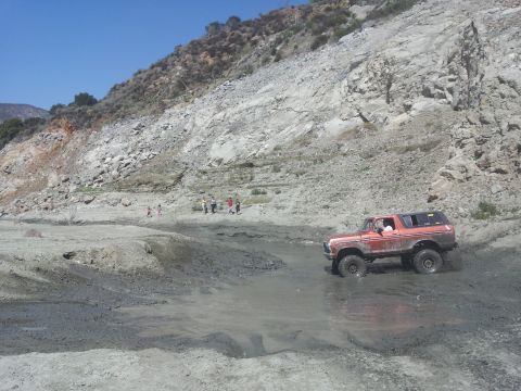 1978 Ford Bronco - This 1978 Ford Bronco navigates a muddy terrain with a steep, rocky hillside under a clear blue sky.