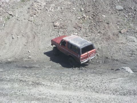 1978 Ford Bronco - This red SUV is navigating a challenging off-road terrain with steep, loose dirt and rocks.