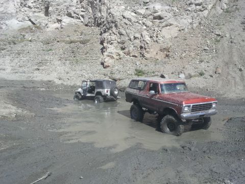 1978 Ford Bronco - Two off-road vehicles, a red 1978 Ford Bronco and a white Jeep, traverse a muddy landscape.