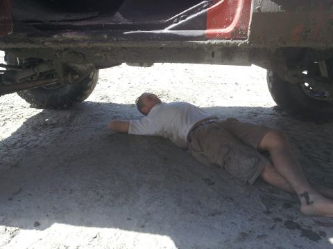 1978 Ford Bronco - A man lies on the ground beneath the chassis of a red 1978 Ford Bronco.
