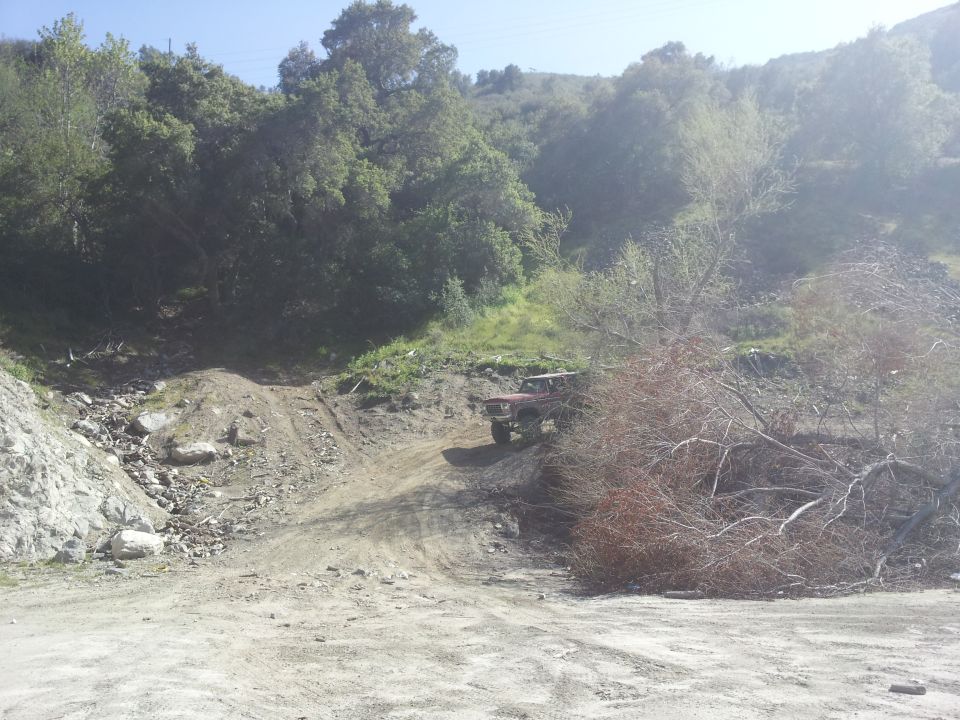 Red off-road vehicle driving up a dirt hill with trees and brush around