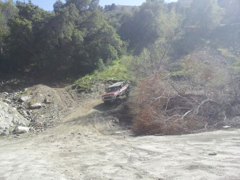 1978 Ford Bronco - A red 1978 Ford Bronco navigates a steep, rocky dirt path in a wooded area.