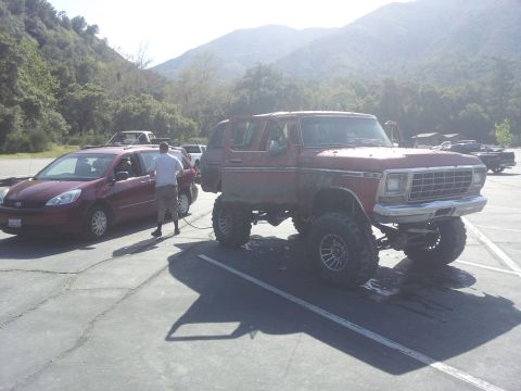 1978 Ford Bronco - A heavily modified 1978 Ford Bronco is parked next to a minivan in a lot with mountains in the background.