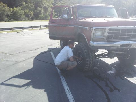 1978 Ford Bronco - A man is airing up the front tire of a red 1978 Ford Bronco.