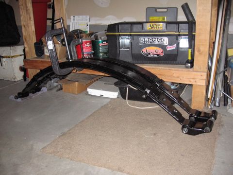 1995 Ford Bronco - Leaf springs are clamped to a workbench, with a toolbox labeled 'Bronco Graveyard' in the background.