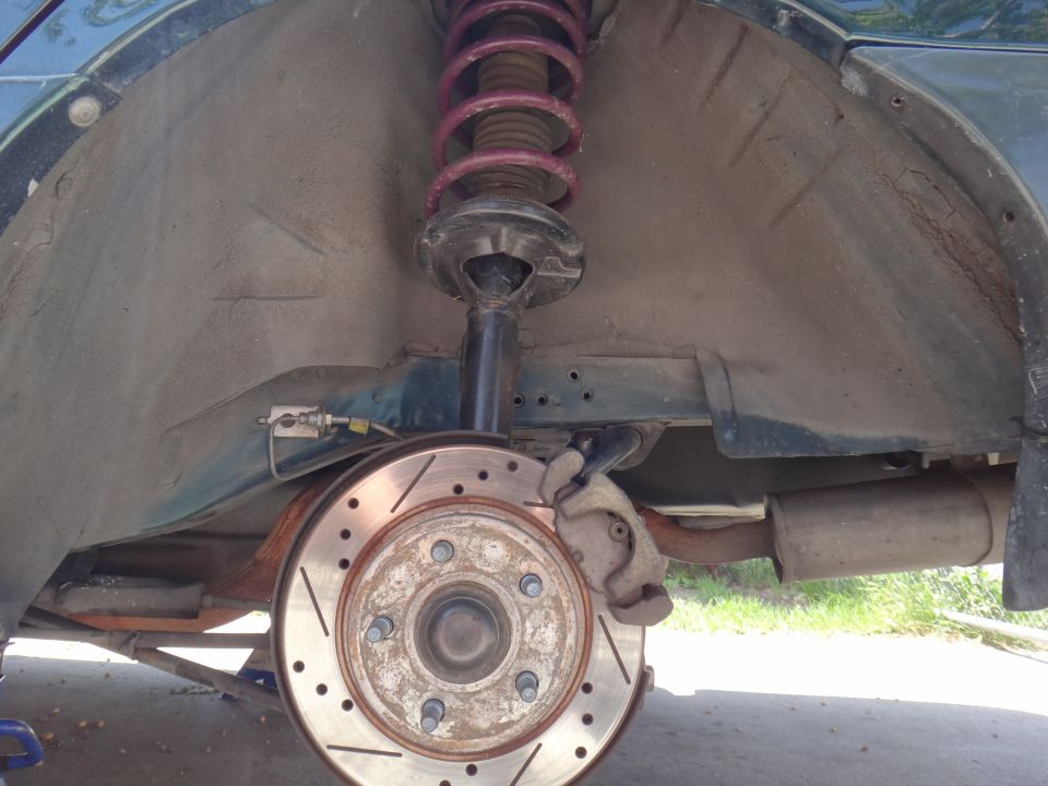 Rear suspension with red coil-over spring and drilled-slotted brake rotor