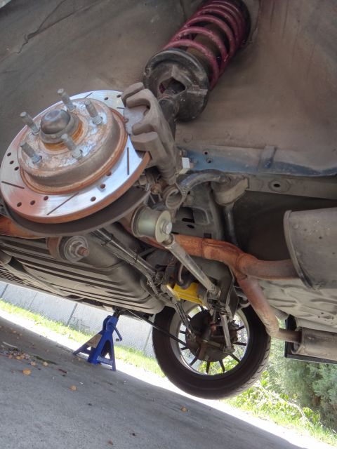 1995 Ford Taurus - Close-up of a car's rear brake and suspension system, showing a drilled rotor and red coilover.
