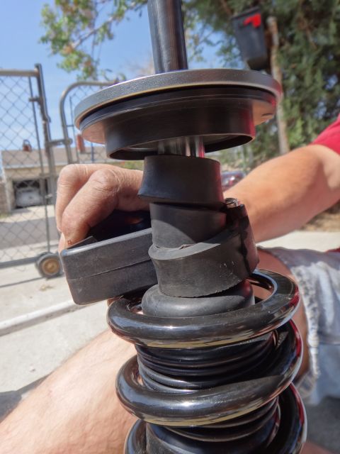 1995 Ford Taurus - A hand adjusts a shock absorber assembly a black coil spring and rubber isolators.