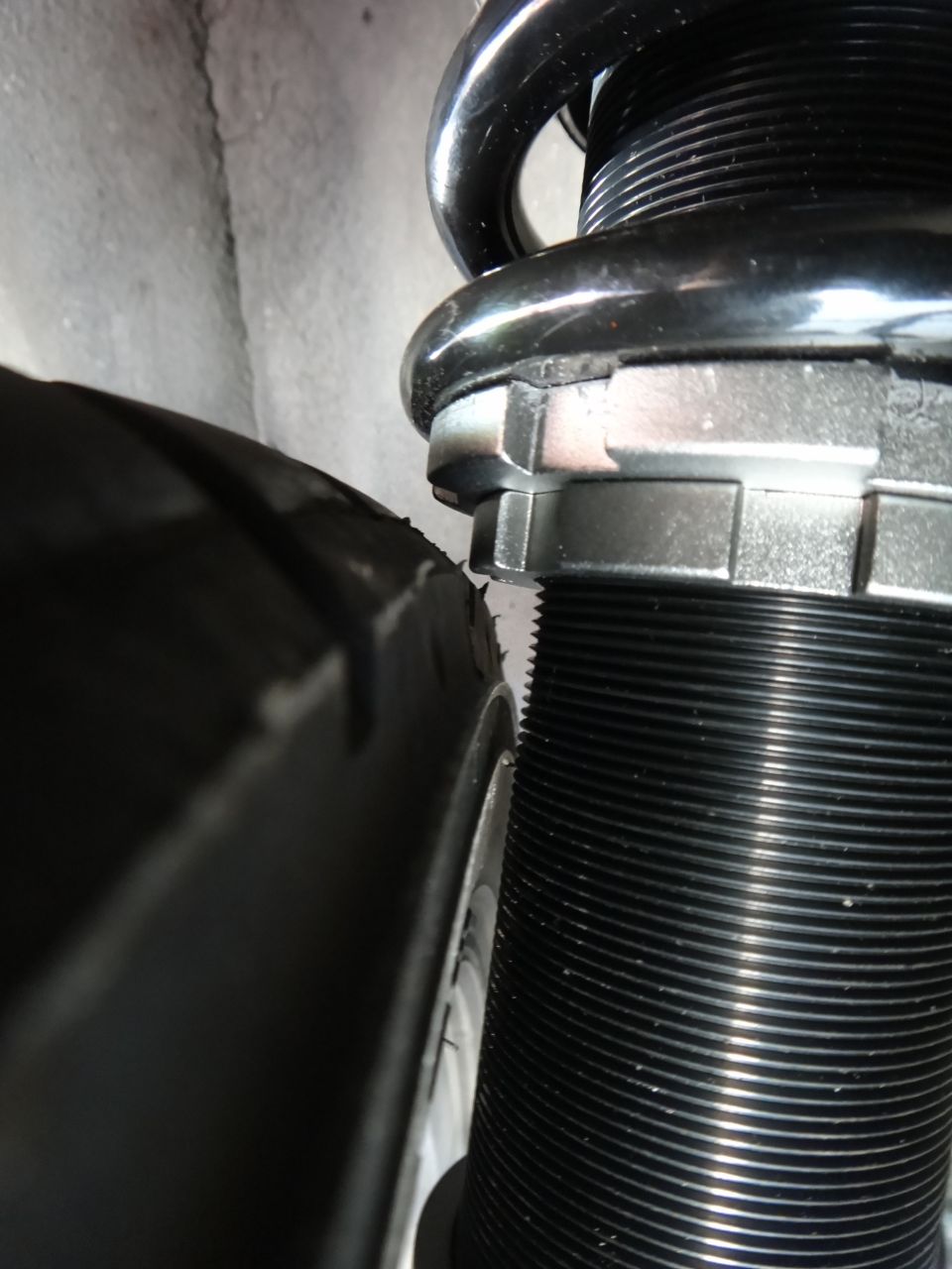 Close-up of a tire next to a black coilover suspension with adjustable spring perch