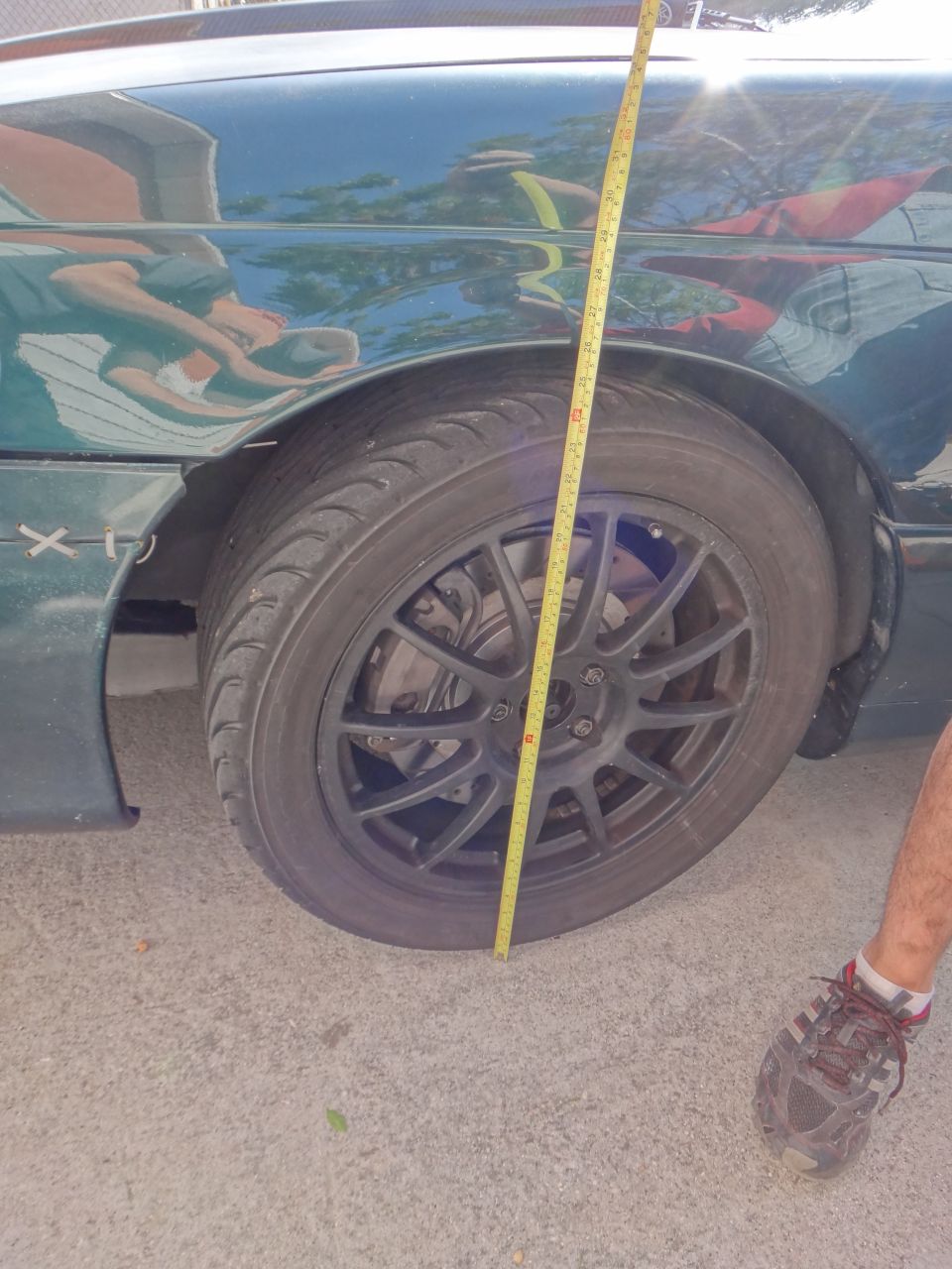 Measuring tape against a dark green car's front wheel and fender