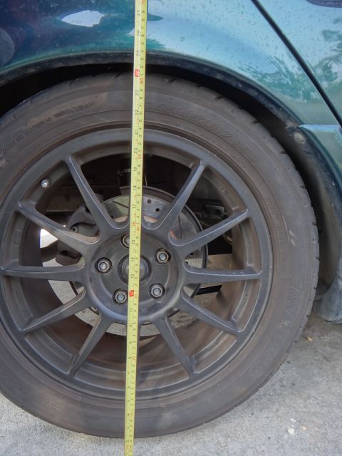 1995 Ford Taurus - A tape measure is used to measure the ride height of a green car's rear wheel and suspension.