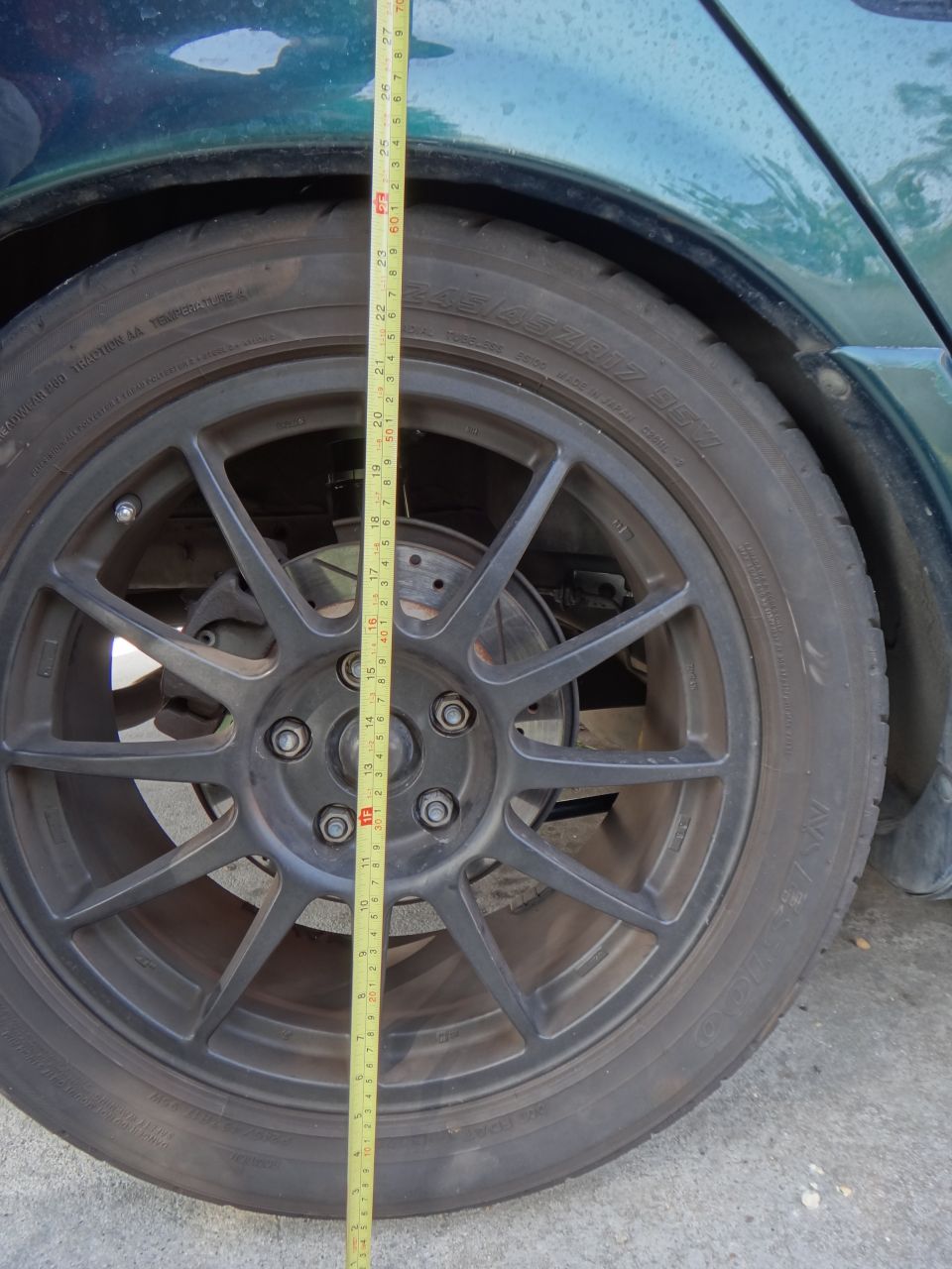 Green car's rear wheel with a tape measure showing ride height